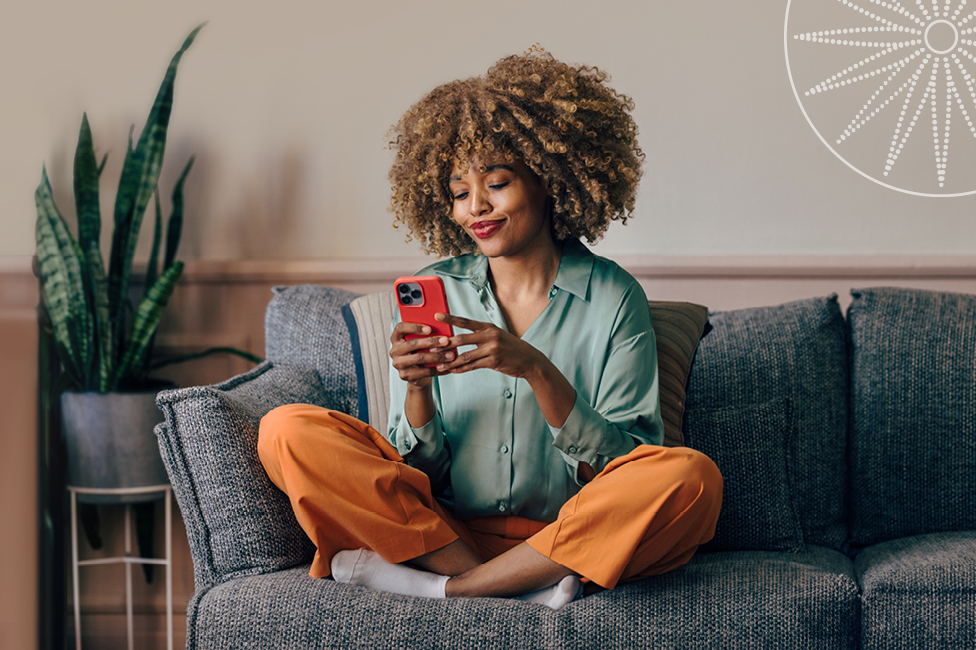young woman sitting on a comfy couch and using her phone
